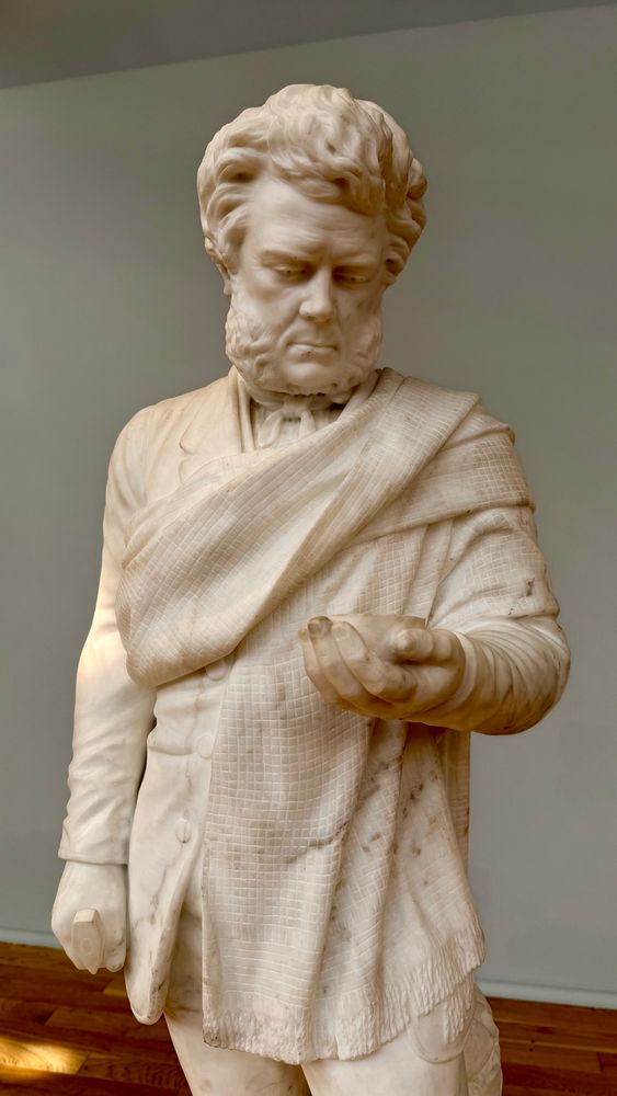 Marble statue of Hugh Miller looking at a fossil fish in his left hand. 