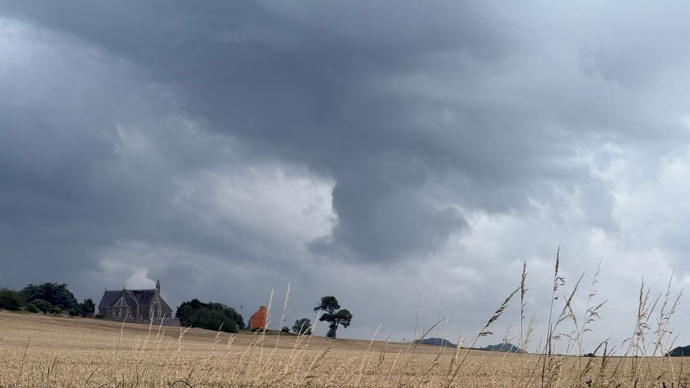 Photograph of a dark, heavy sky above a church and dovecot.