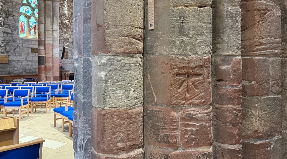 Close view of a red and white sandstone pillar inside a church, with blue seats beyond. The pillar is weathered and has an Ordnance Survey  benchmark cut into it.