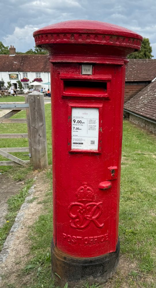 Red pillar box with George VI cypher set into grass on a village green. 