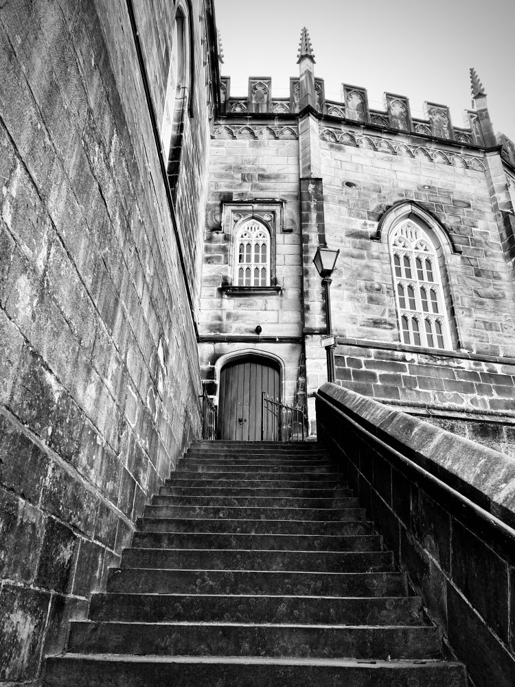 Black and white photo looking up a steep flight of stone stairs on the outside of the castle, leading to another small wooden door beneath some pretty arched windows. They're just good doors brent