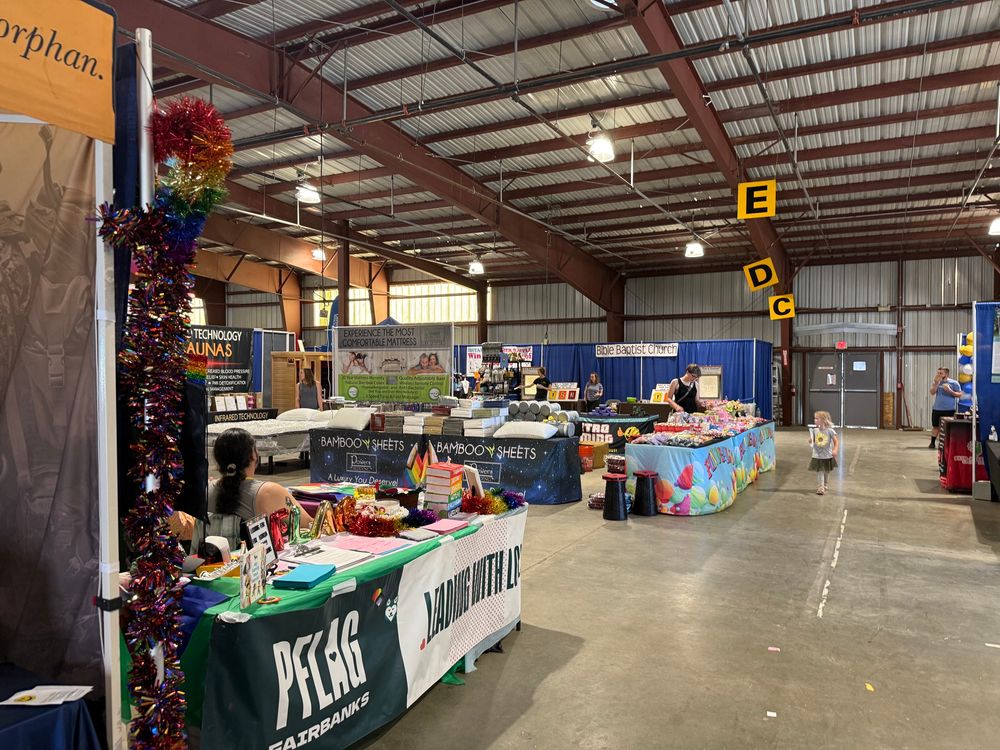 Fair exhibit booths. In the foreground is PFLAG/Fairbanks Pride. In the background, is Bible Baptist Church, who are evil, hateful pedophiles. They are facing each other.