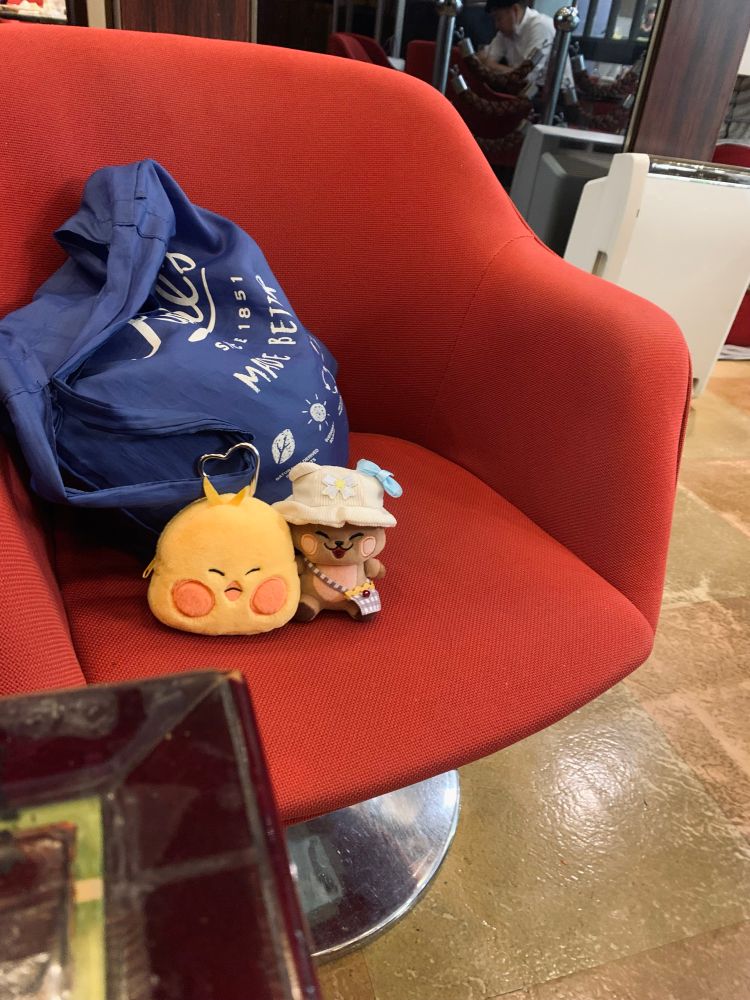 赤い椅子の上に置かれた青い鞄に付けられているヒヨコのポーチの横にリスのぬいぐるみが並んでいる