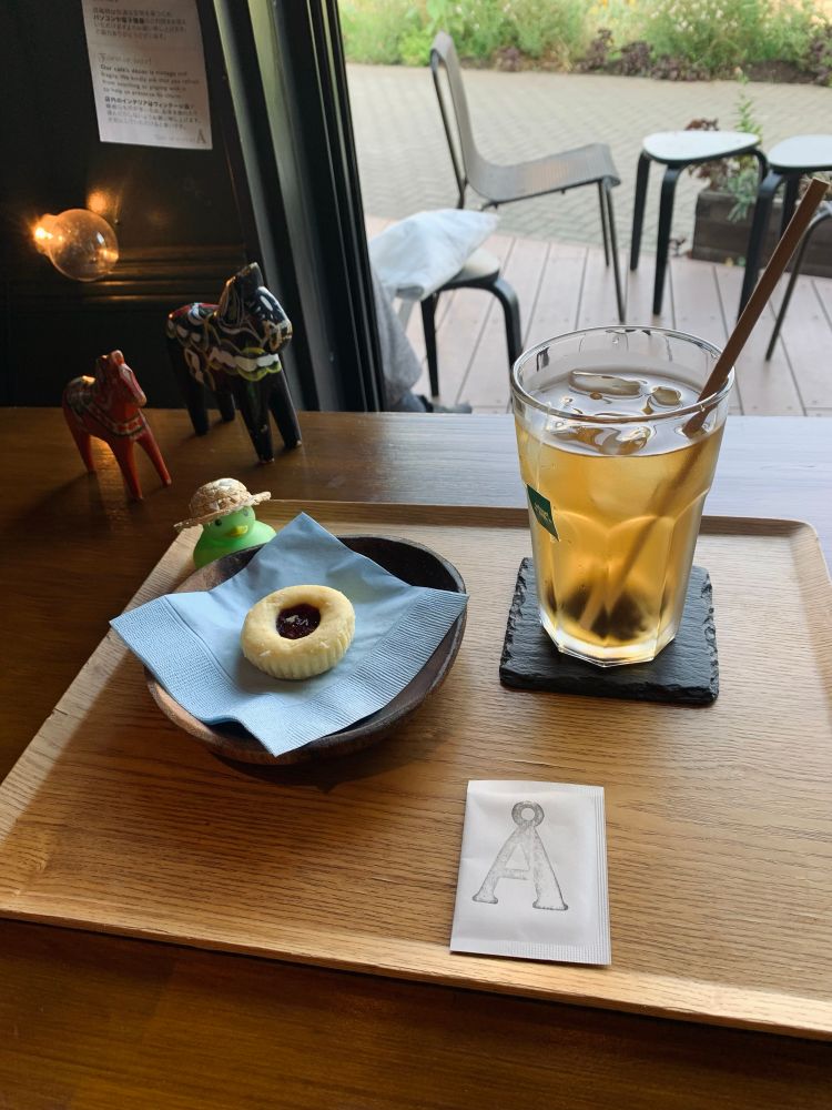 ベリーのジャムが乗ったクッキーと、アイスティーがおぼんに乗っていて、クッキーの後ろに麦わら帽子を被った緑のアヒルの人形が置かれている　さらに奥に馬の置物が二つ並んでいる