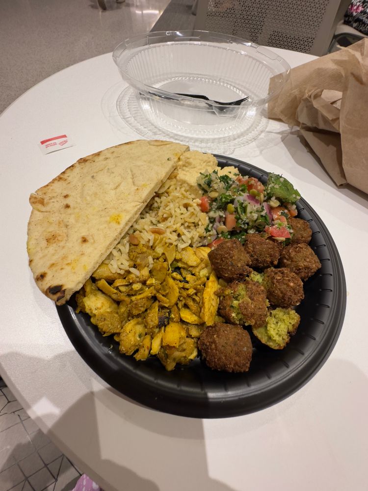 pita, hummus, falafel, chicken shawarma, rice, and tabbouleh on a black plate sitting on a white table 