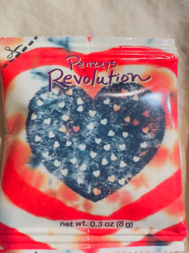 A spice packet that has red and white stripes it is circular pattern around a dark blue heart that has a lot of little multicolored hearts in the center of it. It says it is it resists spice blend.