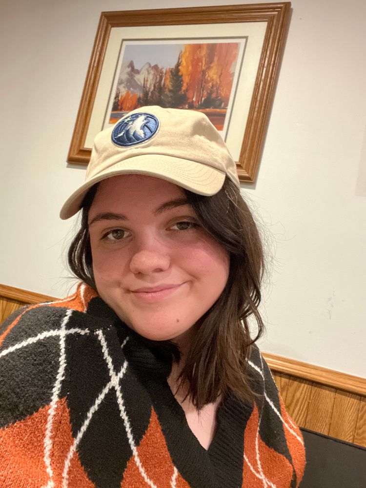 Allie wearing a Timberwolves hat and plaid sweater while smiling 
