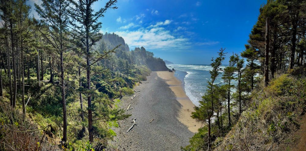 Panoramic shot of a beach in the PNW surrounded by trees and hills in the distance. 