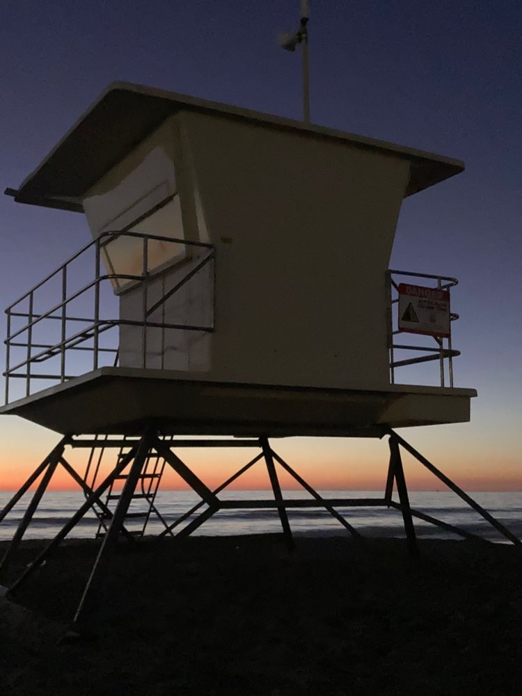 A lifeguards’ station stands silhouetted against the sunset ocean. 