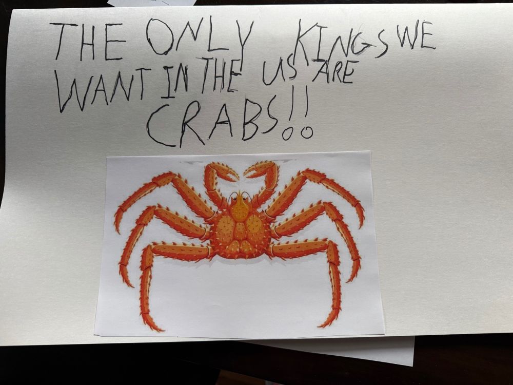 A sign with an image of a king crab saying “THE ONLY KINGS WE WANT IN THE U.S. ARE CRABS!!”