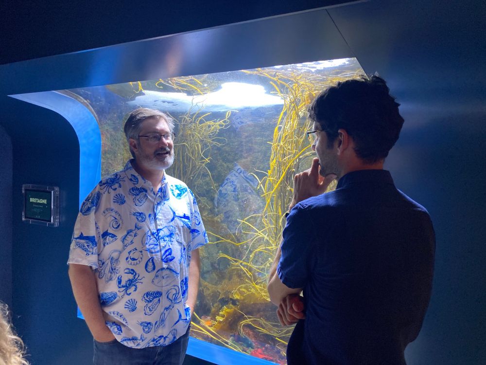 Jarrett Byrnes and John Griffin converse in front of a seaweed-filled aquarium at the International Temperate Reef Symposium gala. 