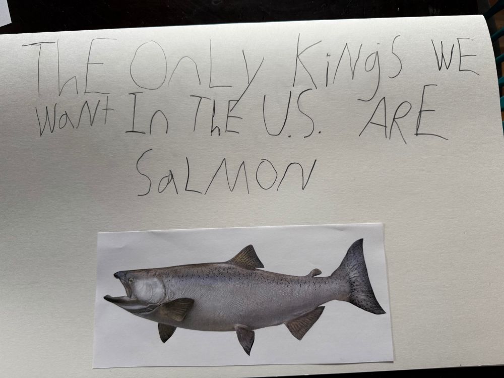 A sign with an image of a king salmon reading, “THE ONLY KINGS WE WANT IN THE U.S. ARE SALMON”
