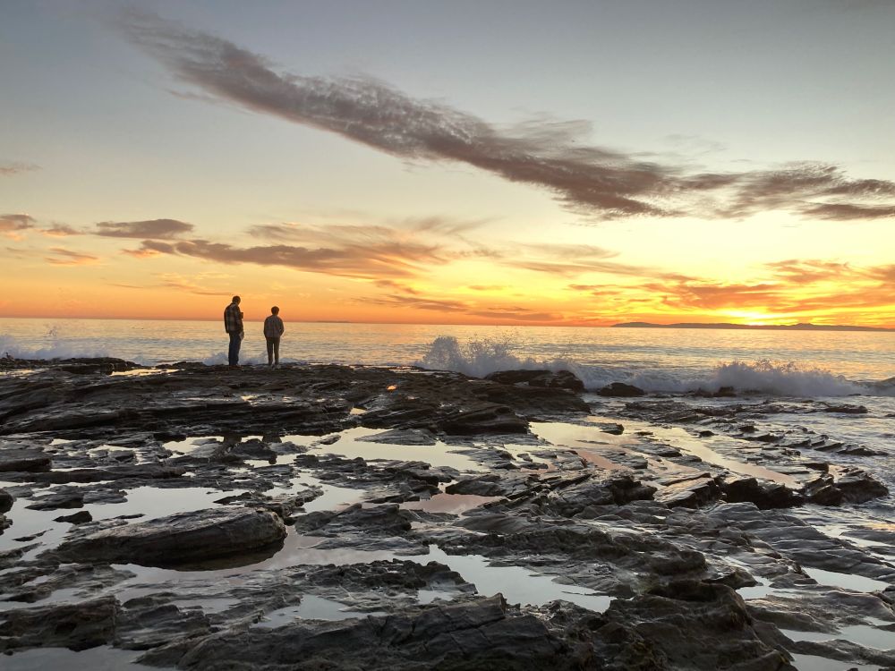 Silhouettes of my boys exploring a rocky intertidal reef against a sunset sky