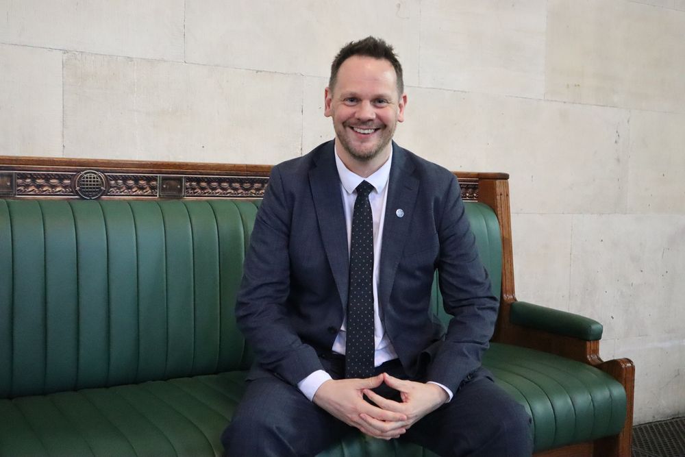 Simon sitting on a replica of the House of Commons green benches