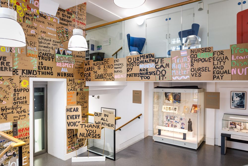 A section of the Art of Nursing exhibition showing a selection of placards with slogans created by RCN members and two display cases with artworks.