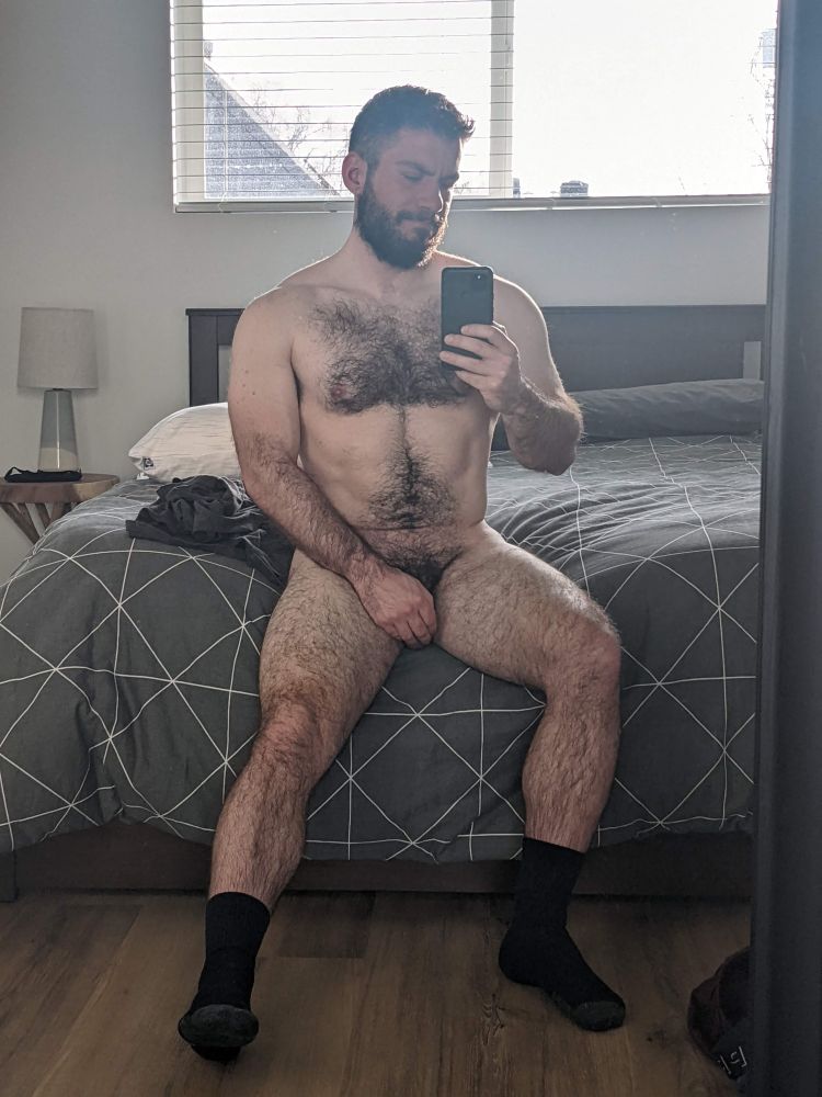 Hairy unclothed man sitting on bed