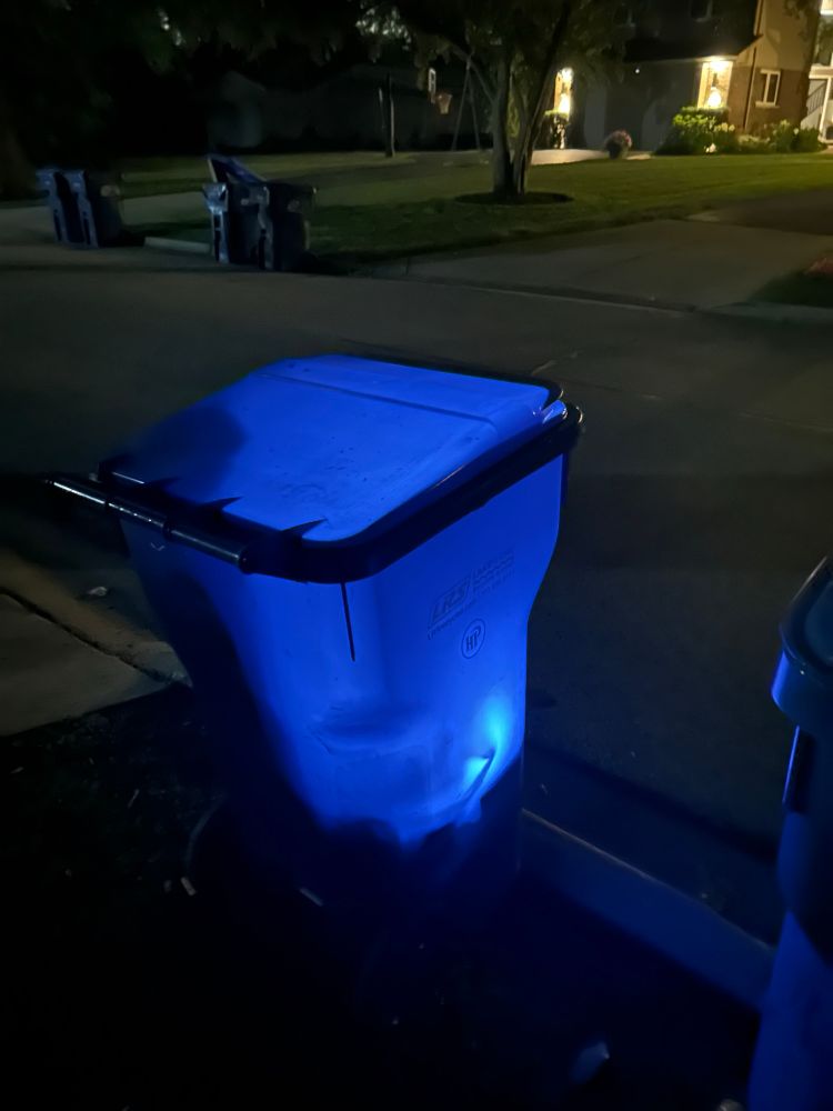 A rolling trash bin at night, glowing with a light inside. 