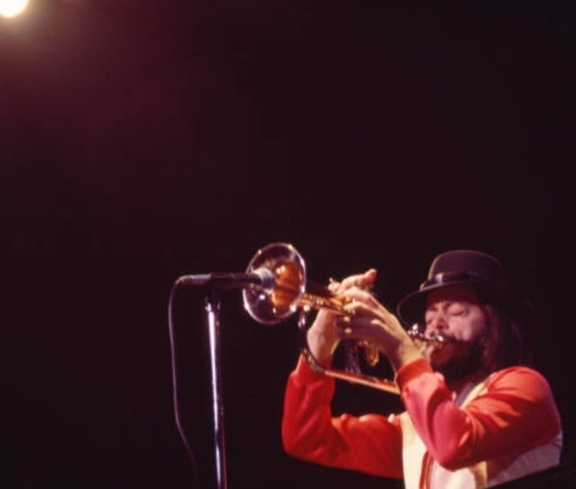 A photo of musician Chuck Mangione playing a flugelhorn in front of a microphone. 