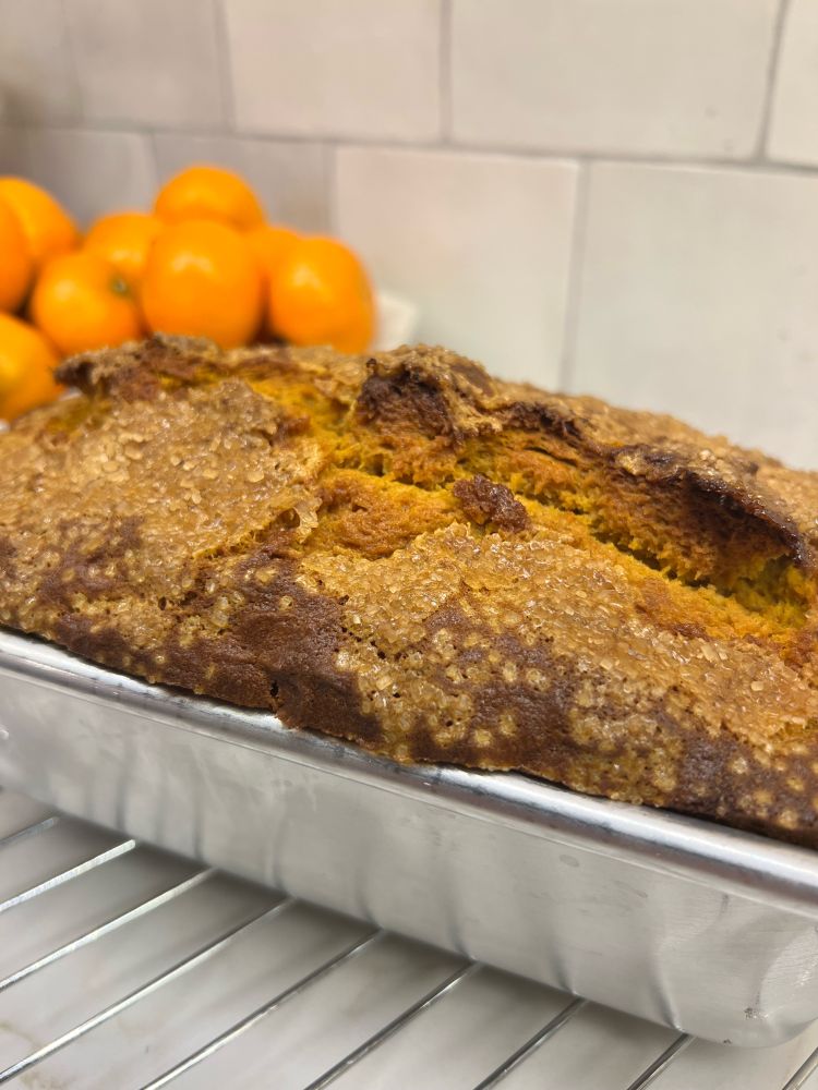 Pumpkin bread on a cooling rack with a bowl of clementines in the background.