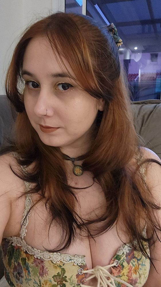 selfie minha, com os cabelos soltos e uma presilha de cabelo, colar marrom e vestido de tecido de sofá de vó (porém fofo). eu estou maquiada e tenho um piercing no nariz