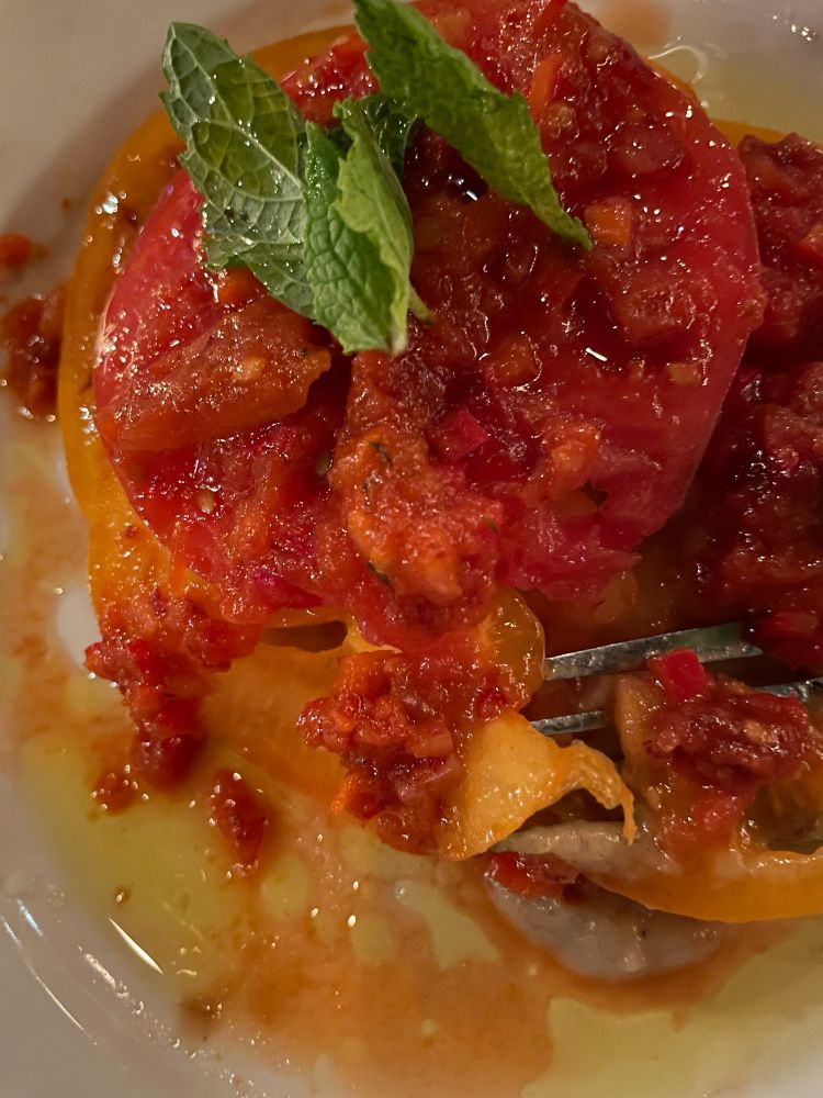 Closeup pic of big bright tomato slices over eggplant puree, topped with relish and mint leaves 