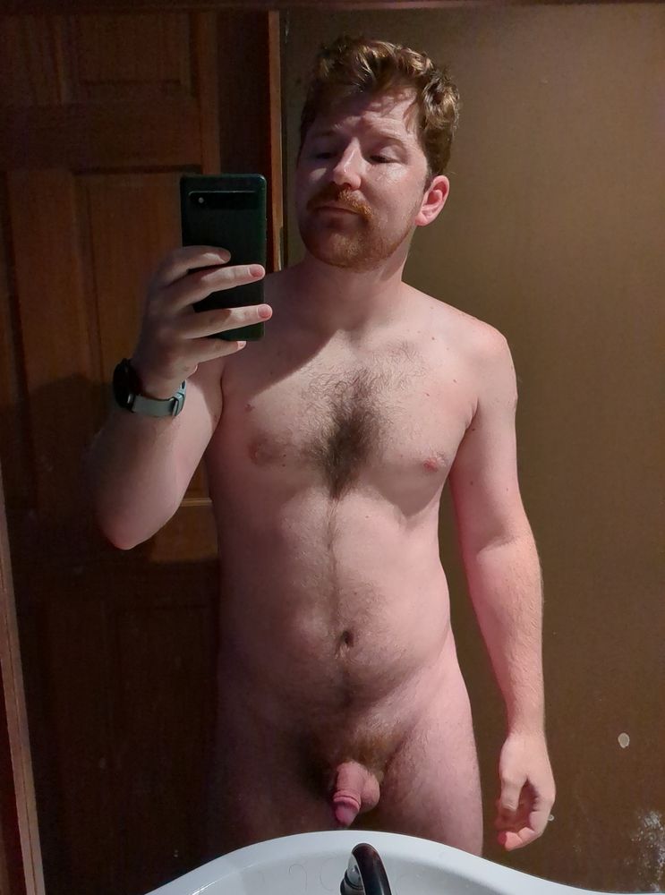 I'm nude and flaccid in the bathroom mirror with only one light on.