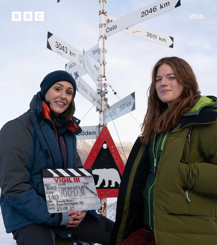 Première photo du tournage de Vigil. Suranne Jones et Rose Leslie posent emmitouflées au Svalbard près d'un panneau directionnel qui pointe des destinations lointaines