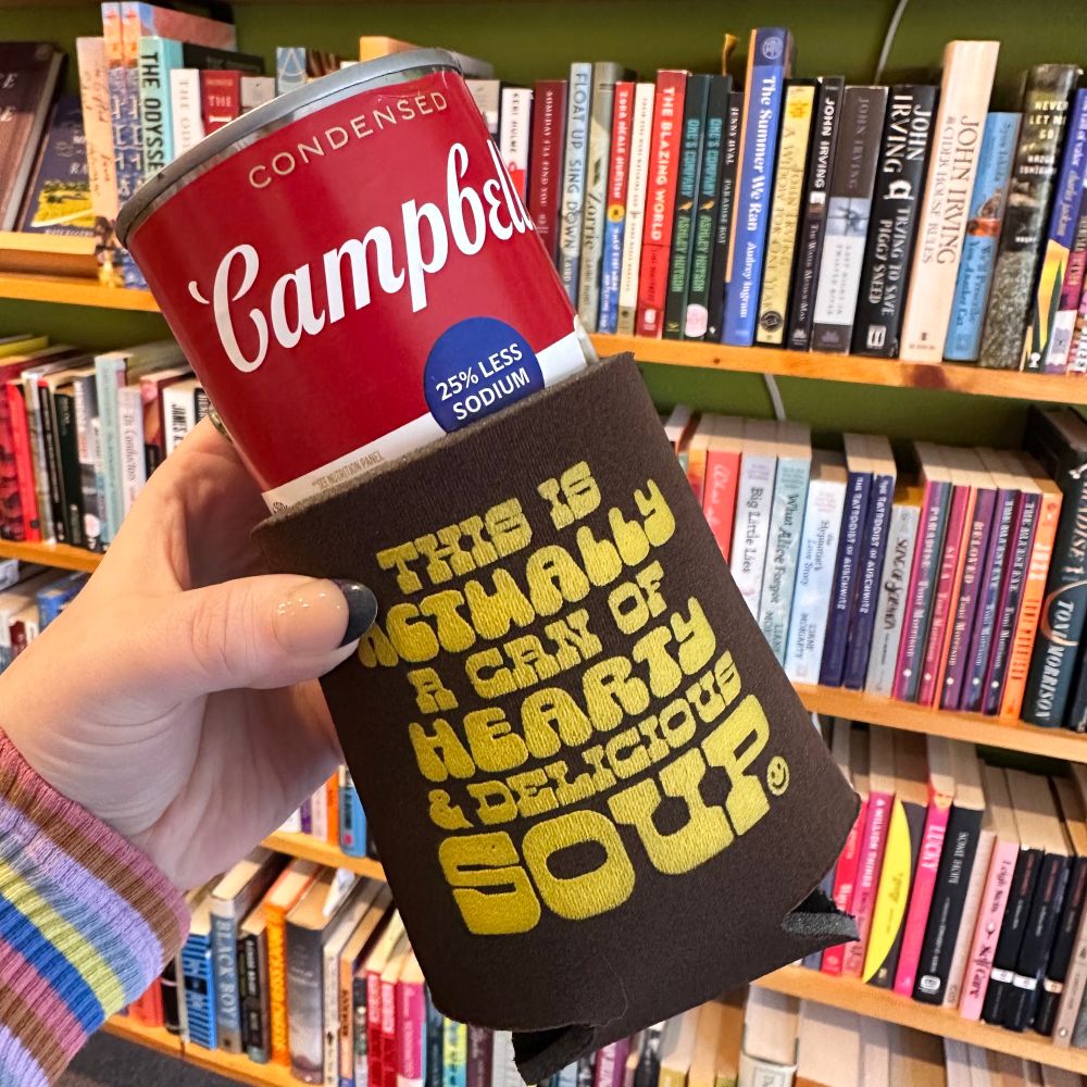 A hand holds up a foam koozie that says THIS IS ACTUALLY A CAN OF HEARTY DELICIOUS SOUP with a campbells soup can sticking out the top