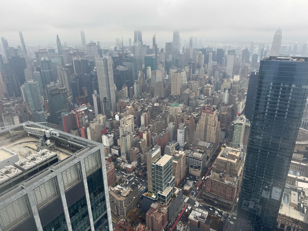A view of New York City from the top of a skyscraper. The sky is cloudy and there is a thick fog in the distance.