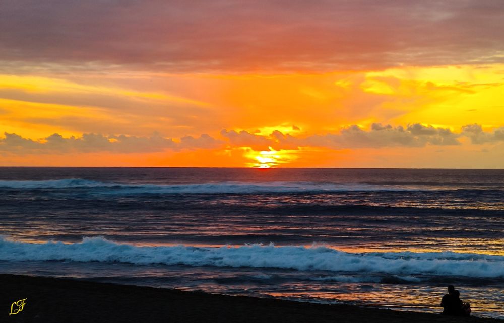 Coucher de soleil sur l'océan indien. Le ciel est jaune et orangé. Le soleil couchant est, en partie, caché par les nuages. Les couleurs se reflètent sur l'océan.  