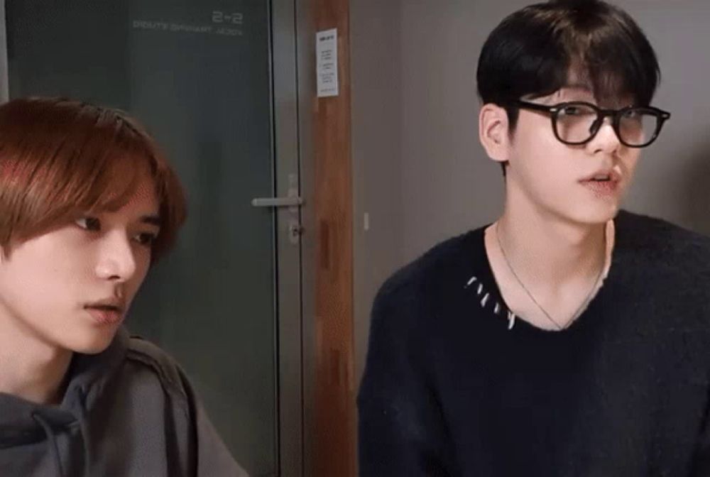 a man wearing glasses and a black sweater looks at another man