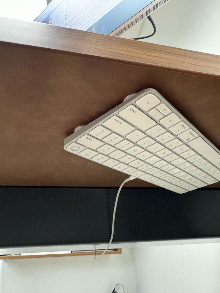 An Apple Magic Keyboard fixed to the underside of a desk