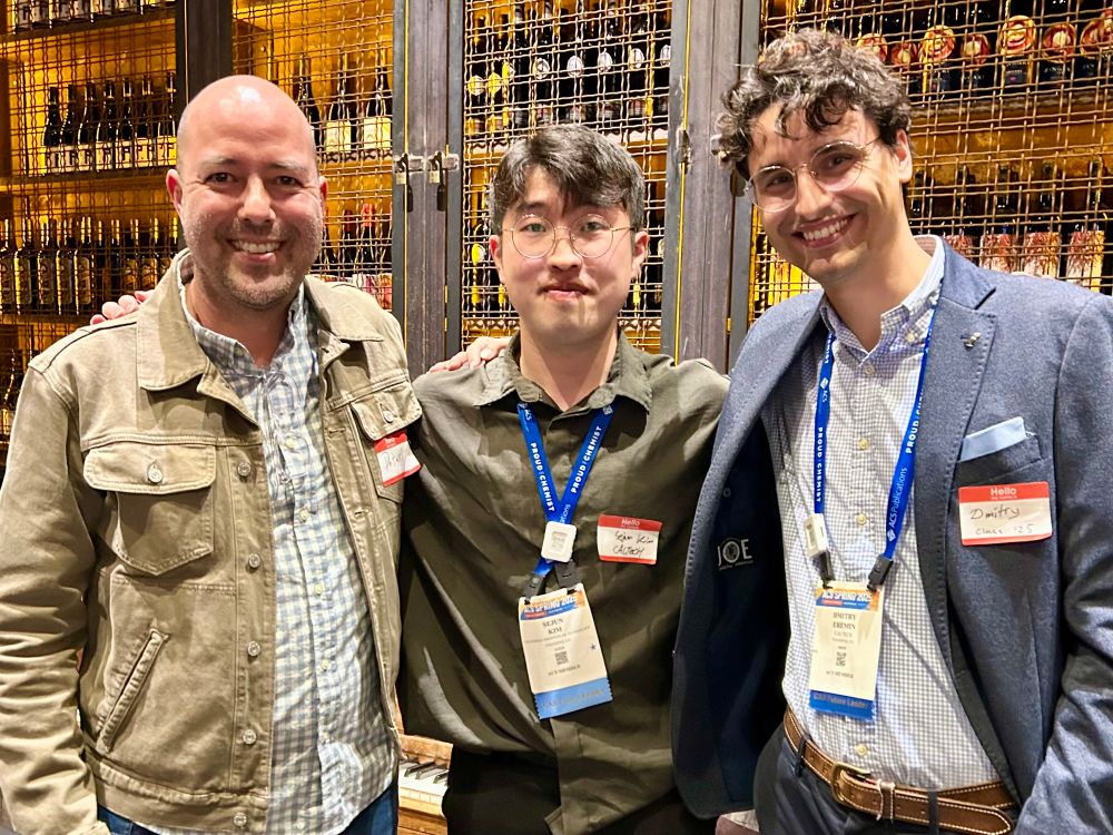 Peter, Sejun, and Dmitry standing in front of a wall of bottles at a restaurant. 