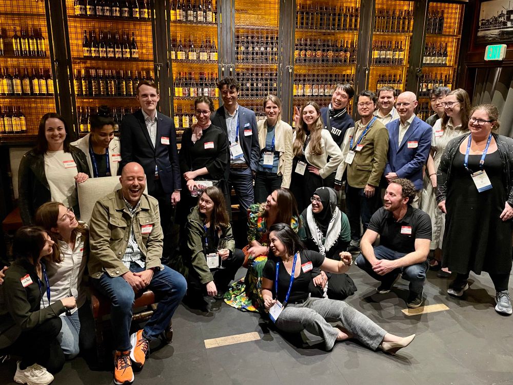 Group of early-career scientists posing in front of a wall of bottles. 
