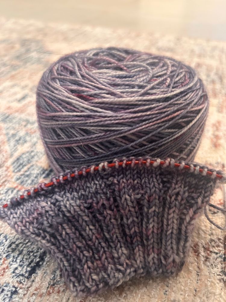 A ball of yarn with the start of a knitted sock