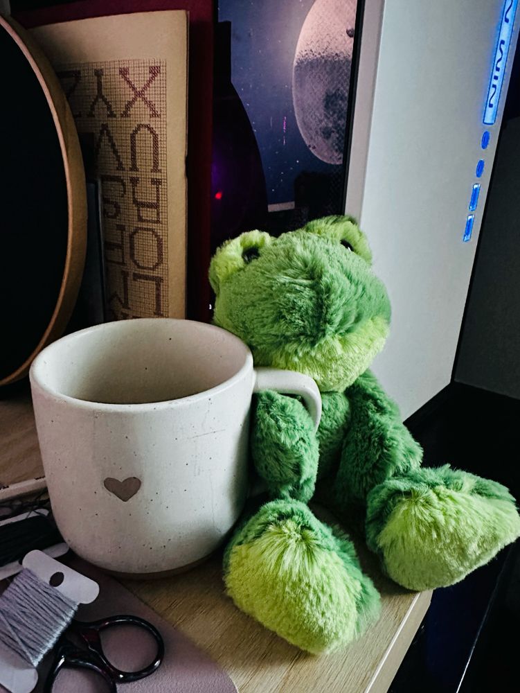 A cute frog stuffed toy holding on to a coffee mug. 