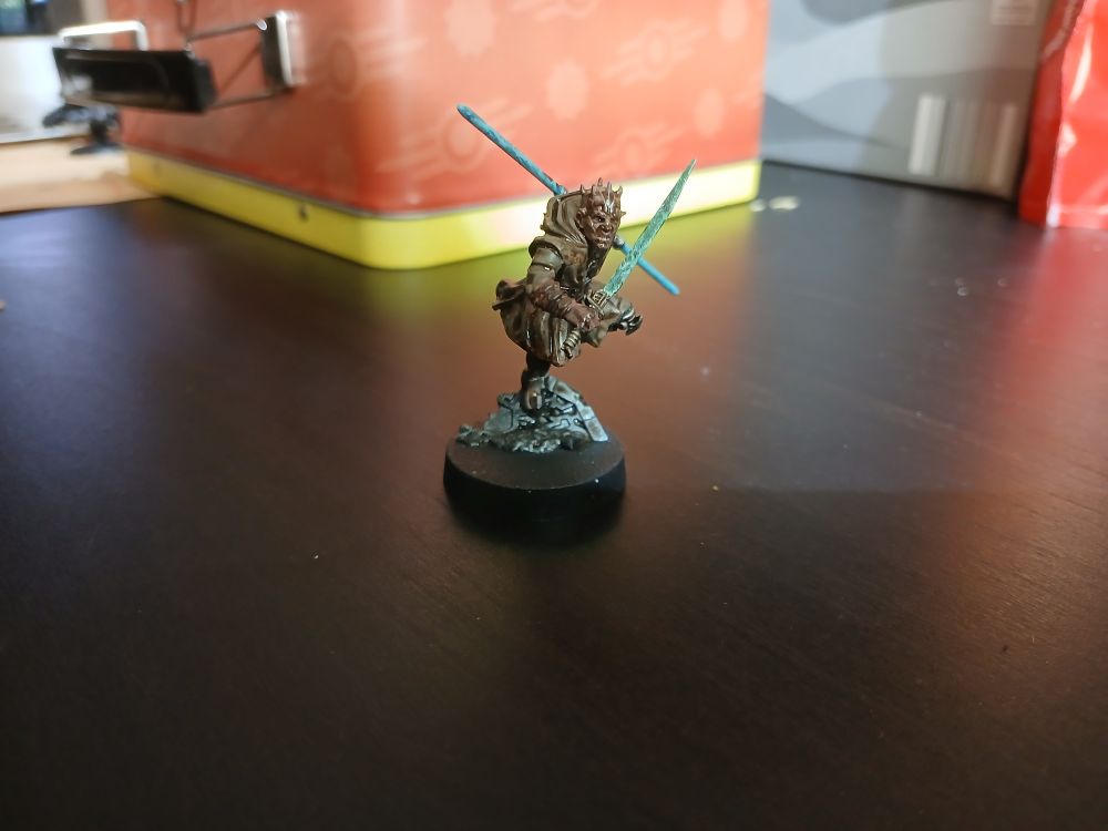 Maul, a rival miniature from star wars legion miniatures game. He is painted in the style of a zabrak jedi master with a blue saberstaff and green lightsaber. He has the a tan zabrak skintone, and the traditional brown Jedi robes with silver armouring.