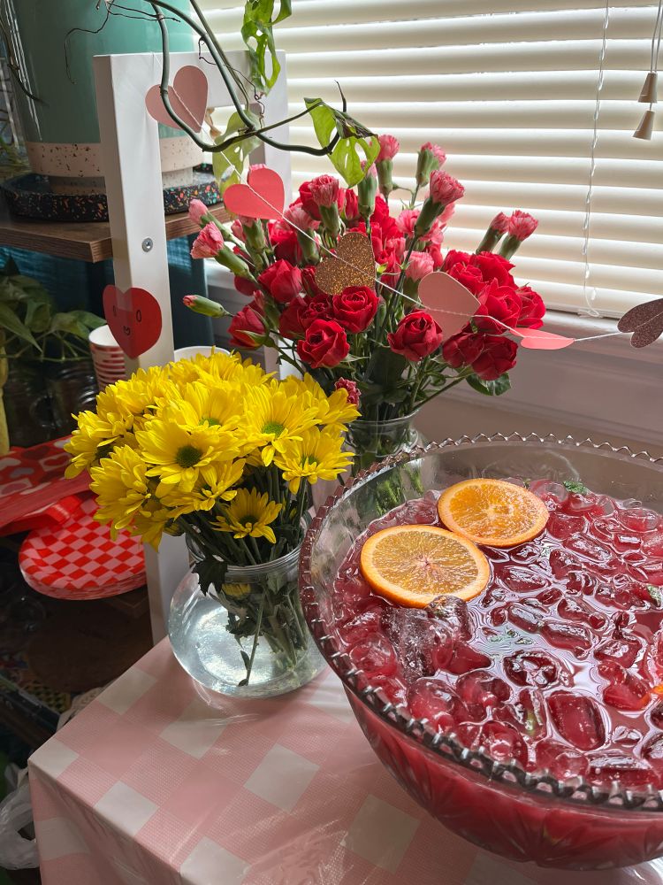 two vases of flowers and punch bowl full of punch and orange slices