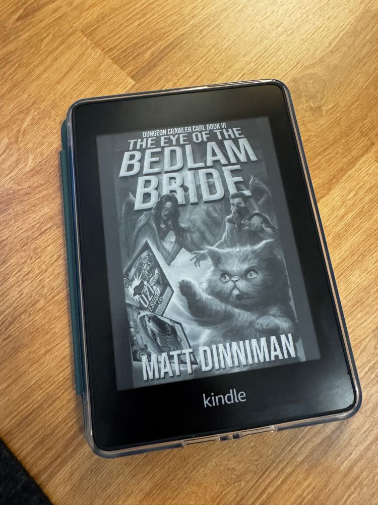 Photo of a kindle on a wooden table showing the cover of the book “The Eye of the Bedlam Bride” by Matt Dinniman