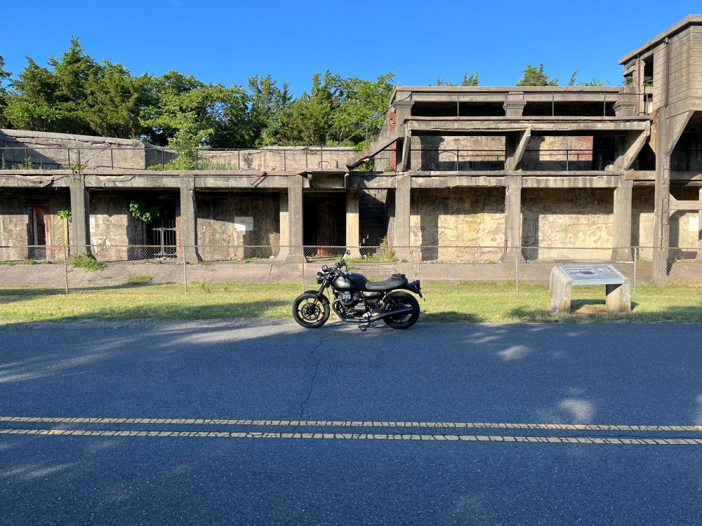 All black moto guzzi v7 stone motorocycle parked in front of the old artillery bunkers at Sandy Hook, NJ. Wide shot, summer. Guzzi looks rad AF.