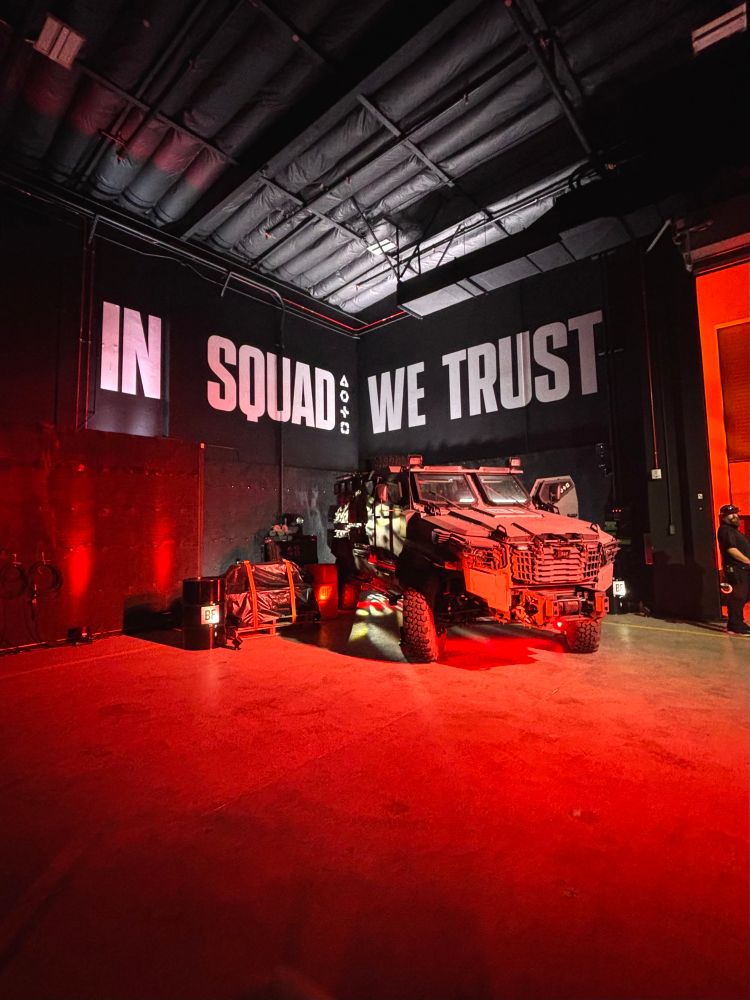 Military vehicle display at Battlefield 6 Multiplayer Reveal event. On the wall behind are the words “In Squad We Trust”.