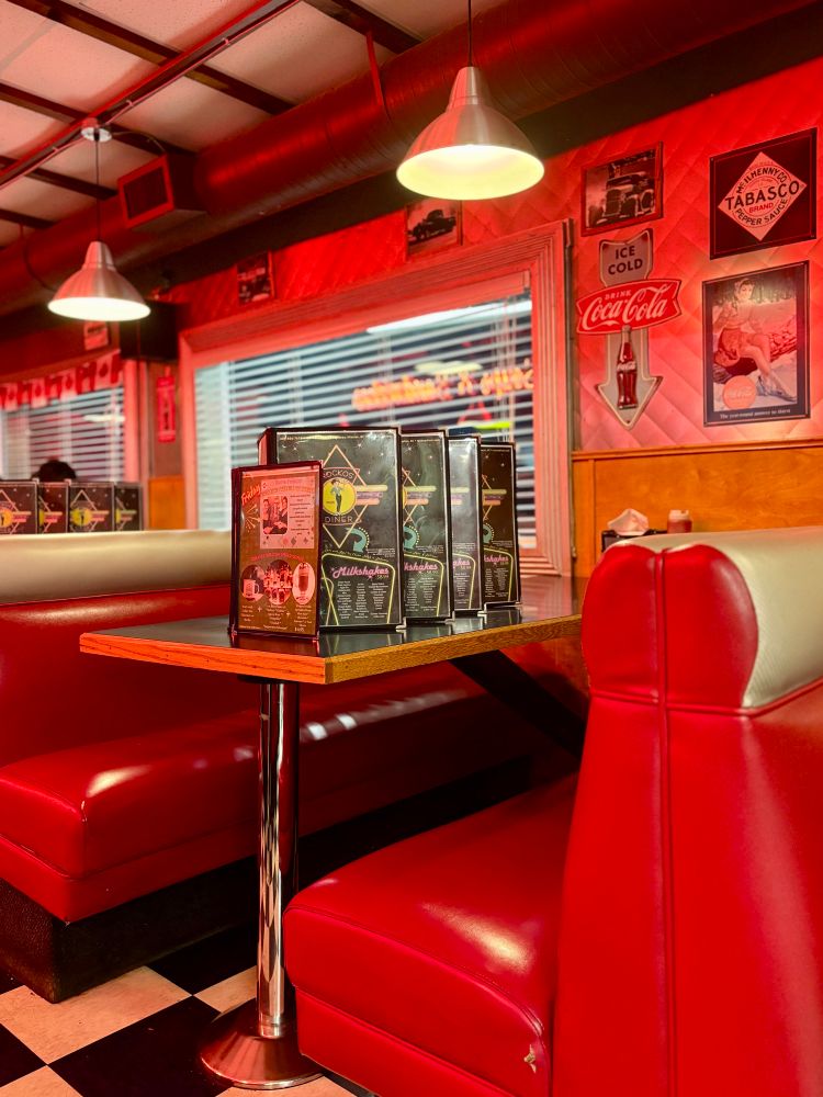 Interior of Rocko’s diner in Mission, BC; an empty booth with plush red chairs, checkered floor, and red-tinted lighting