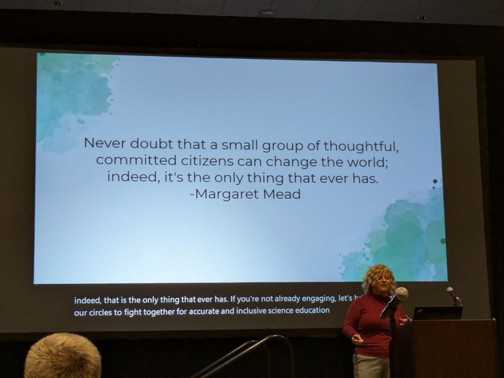A woman standing in front of a podium at a conference. The slide behind her has a quote by Margaret Mead that says "Never doubt that a small group of thoughtful, committed citizens can change the world: indeed, it's the only thing that ever has." 