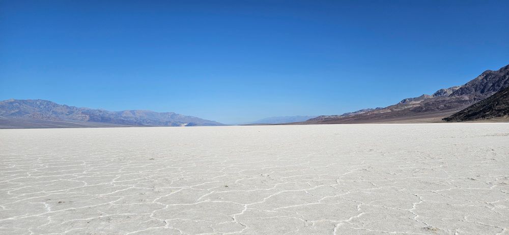 A view of the Badwater Basin area showing a semi-infinite flat plane of featureless salt. Well, not really featureless: the salt forms rough geometric puddles with raised edges. BTW, lowest spot in North America, 85m below sea level.