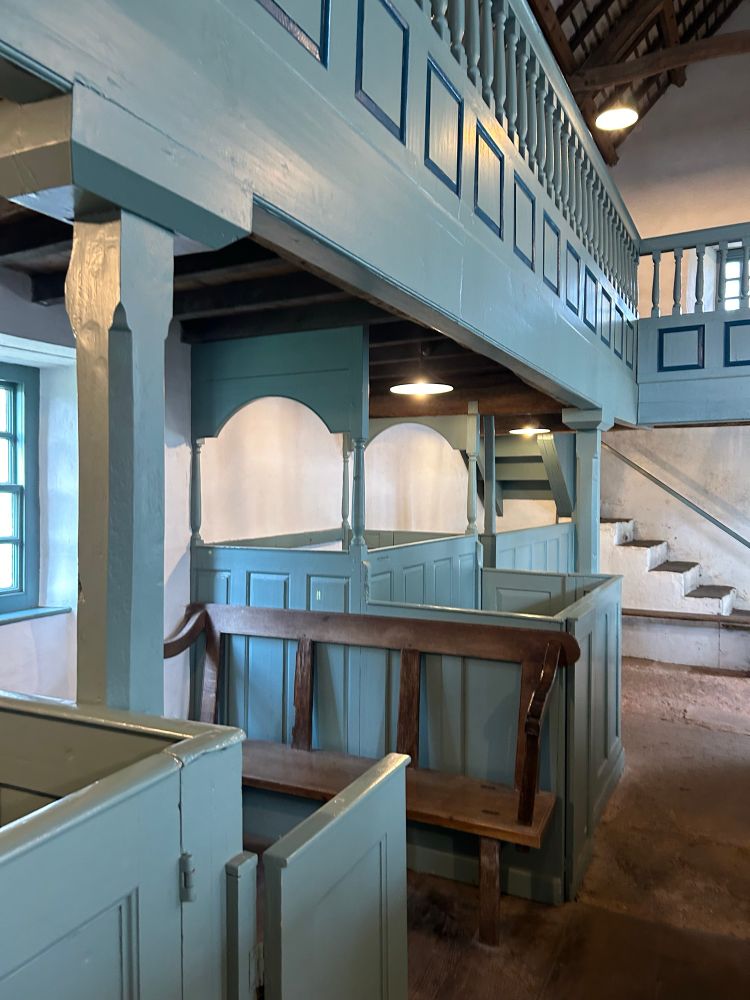 Box pew painted soft grey green beneath gallery with fielded and raised panelling. Stone stairs with slate flag to first floor.