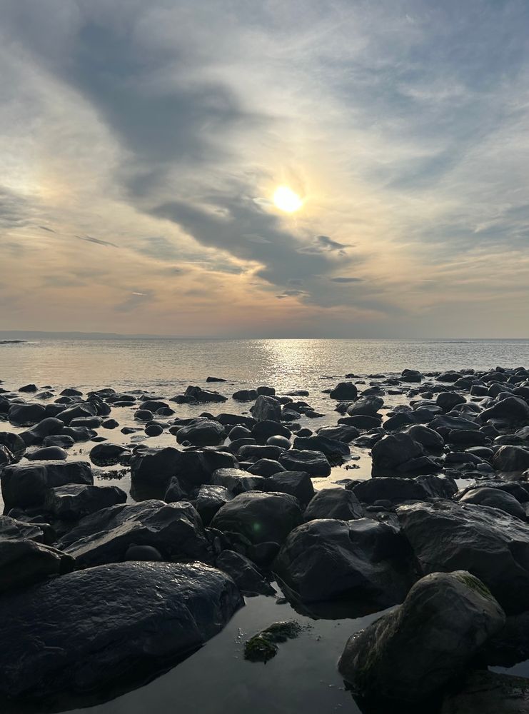 A calm sea and a pebbled beach at sunset, rock pools in the foreground