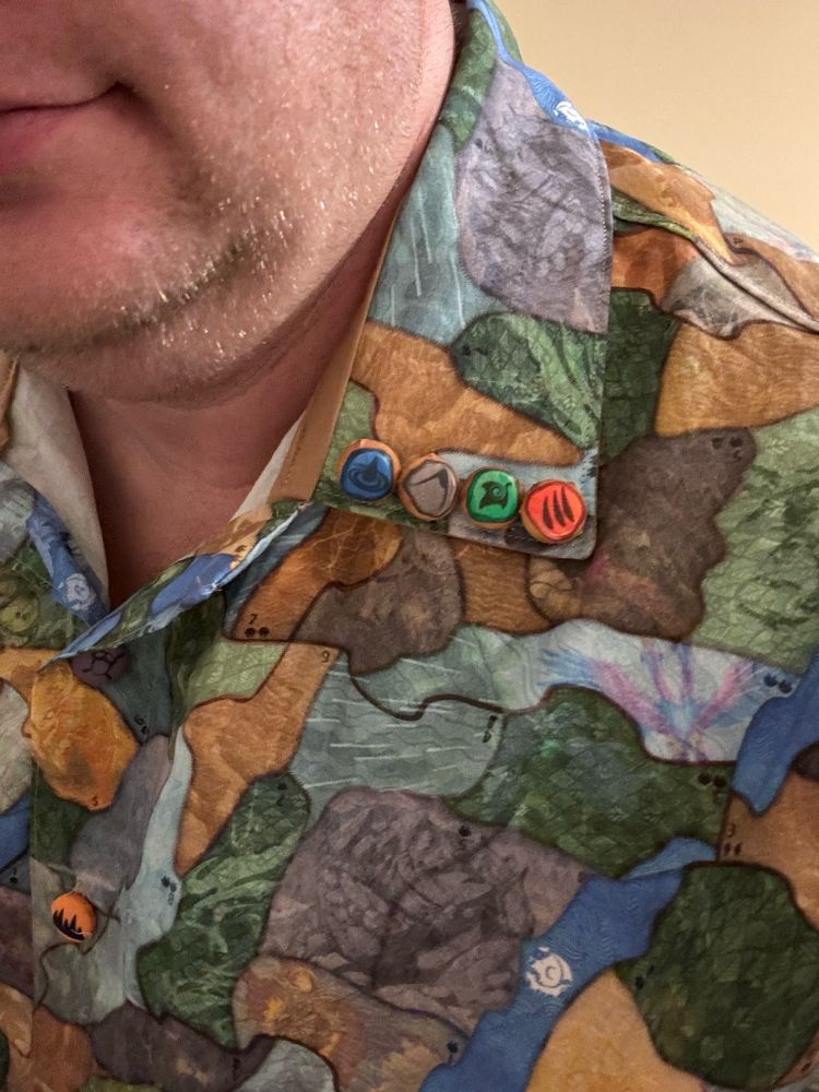 A close up of the collar of a shirt, centering shank buttons featuring the icons for the water, earth, plant, and animal elements from Spirit Island.