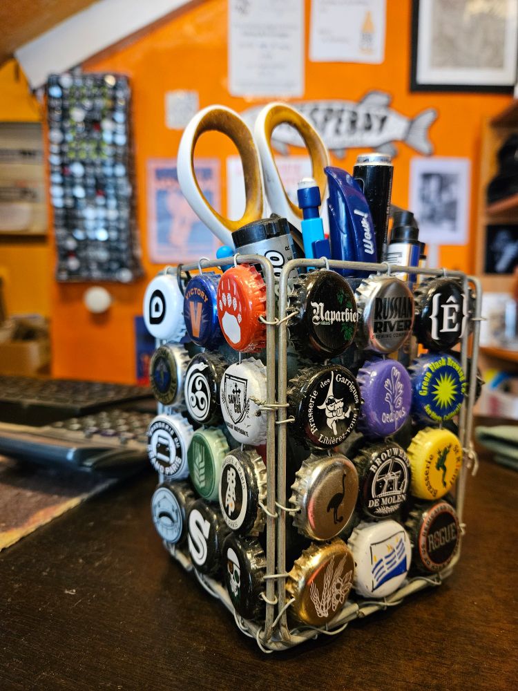 Porte stylos d'environ 10 cm de haut et 8 de large fait avec des capsules et un grillage en fil de fer. Derrière, un panneau de 60 cm de hauteur et 25 cm de large fait également avec des capsules reliées entre elles par du fil de fer.
