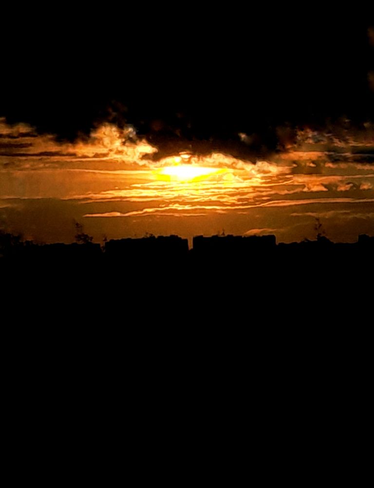Закат скрытый за облаками, но словно вверх ногами. Видно силуэты облаков и домов, а также немного деревьев.