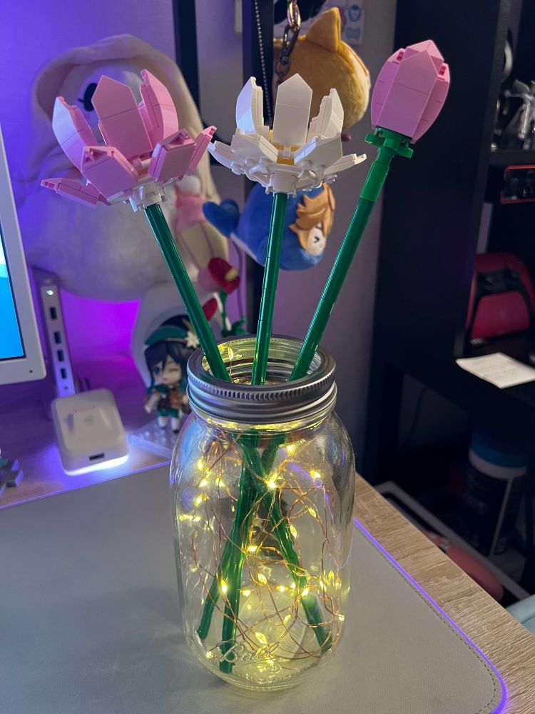Pink and white lotuses built from legos are in a mason jar. Fairy lights decorate the inside of the jar.